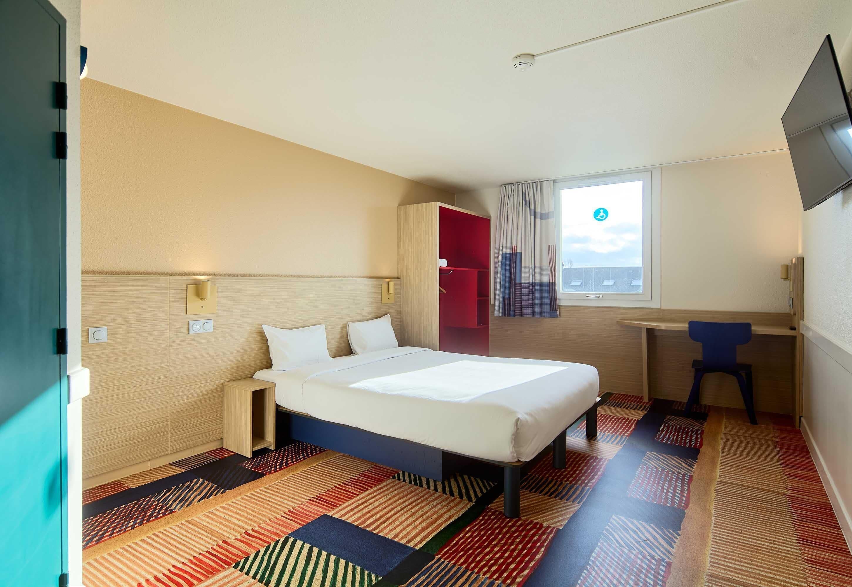Une chambre d’hôtel avec un lit, un bureau, une télévision et une fenêtre avec des rideaux.