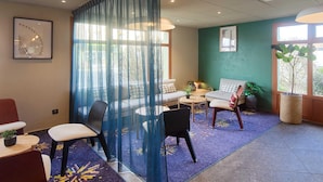 Una habitación con una cortina azul, un sofá, una silla, una mesita y una planta en maceta.