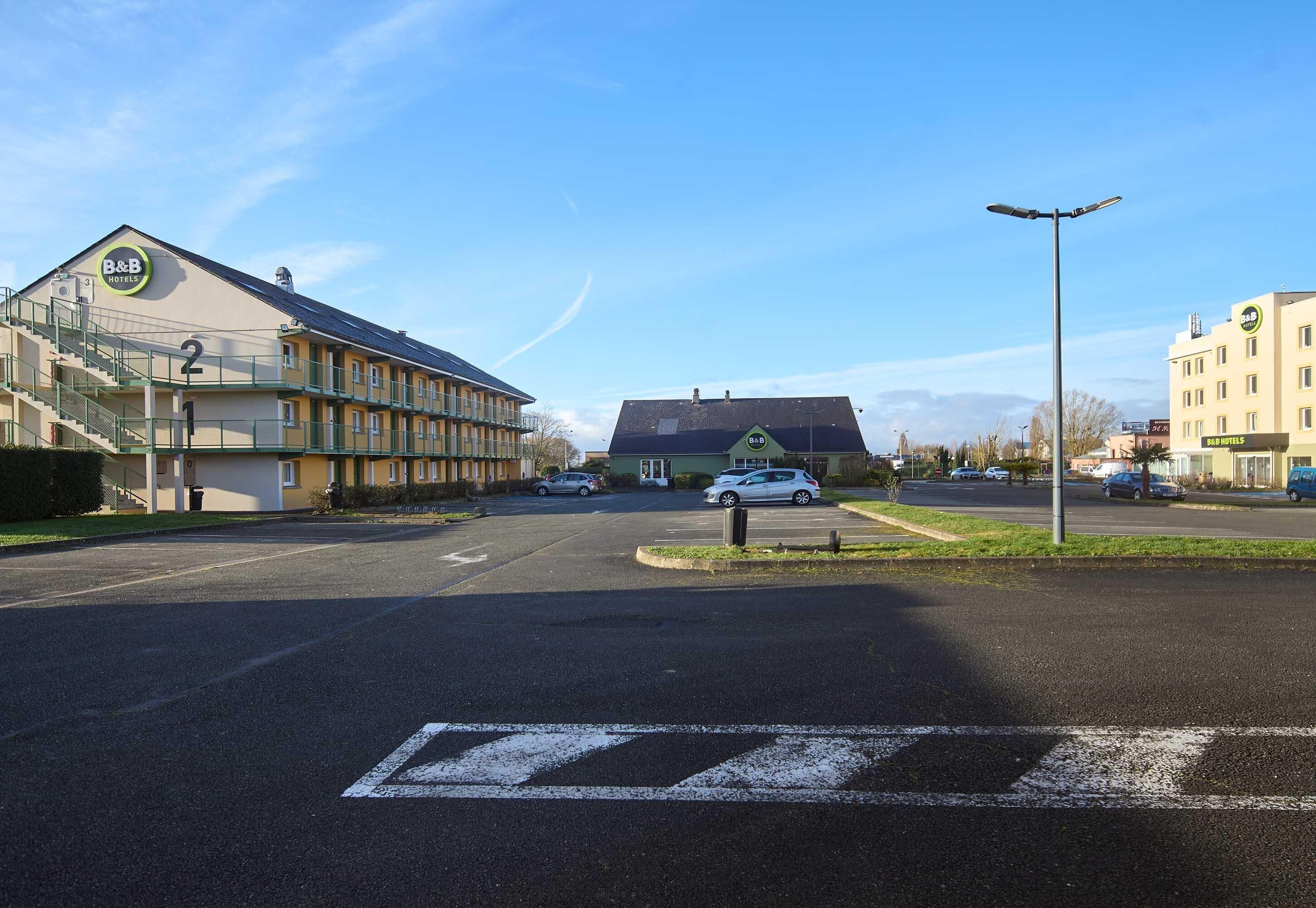 A B&B hotel with a large parking lot, a pedestrian crossing, and a street with cars.
