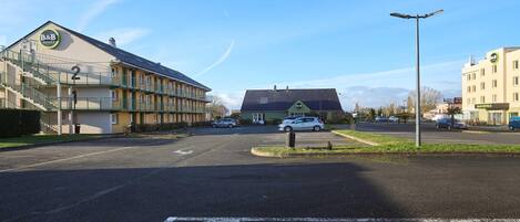 A B&B hotel with a large parking lot, a pedestrian crossing, and a street with cars.