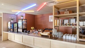 Zona de recepción de hotel con mostrador, máquinas de café, vitrina refrigerada y diferentes alimentos.