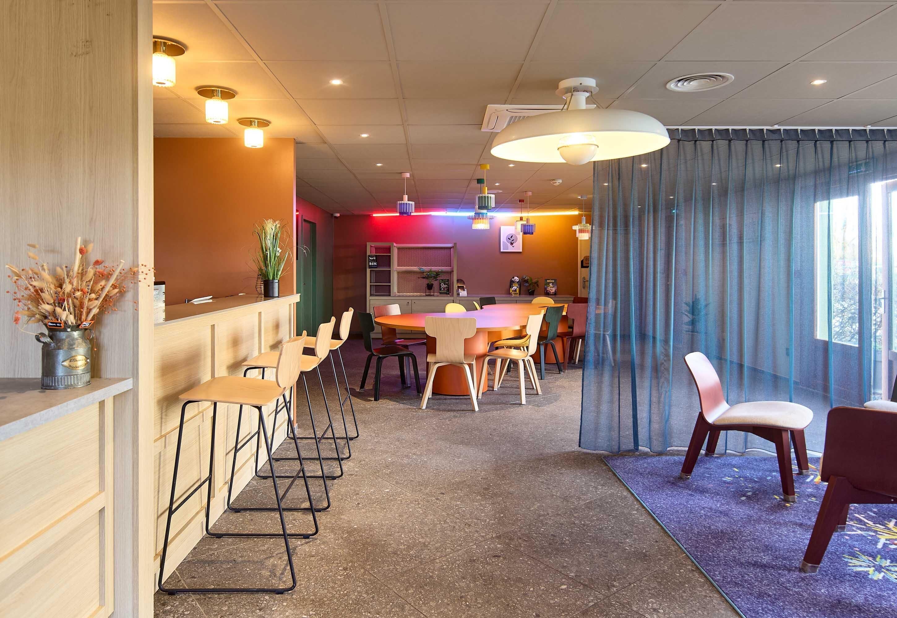 A hotel lobby with a reception desk, multiple seating areas, and a large window with curtains.