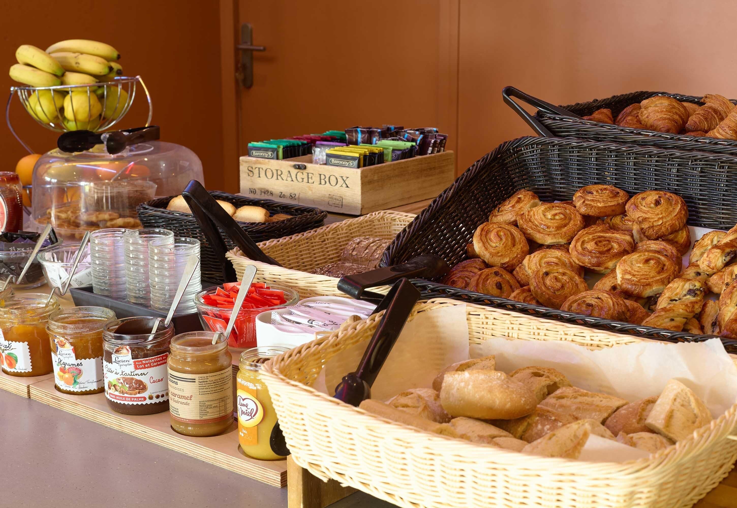 A buffet table with various food items, including pastries, fruits, and condiments.