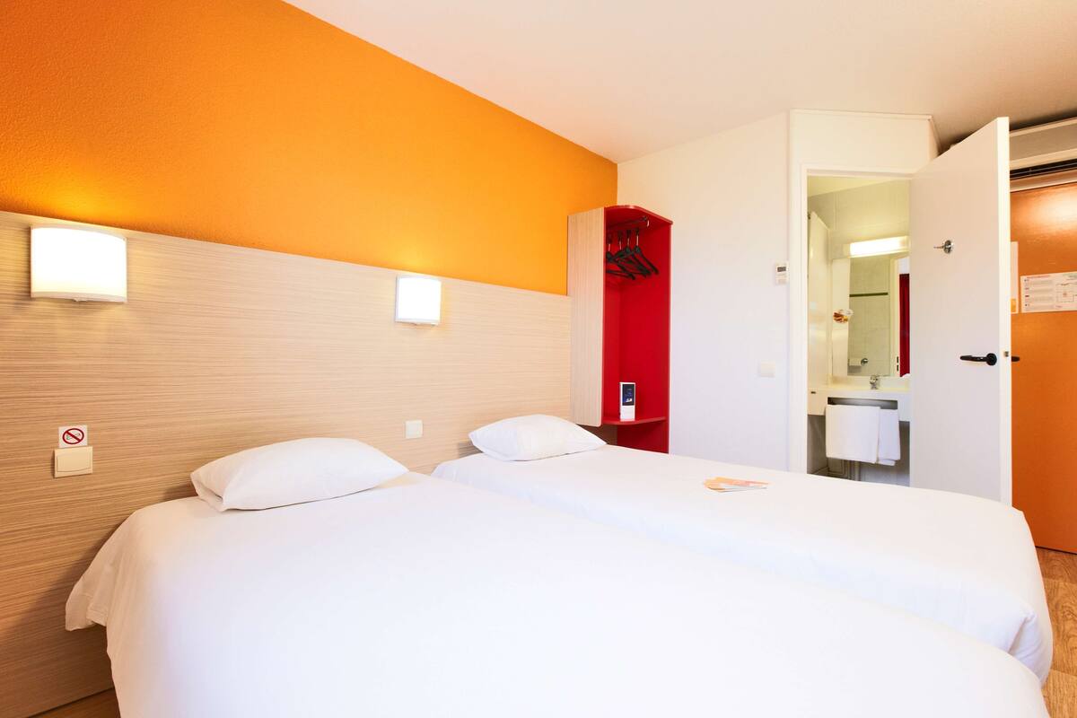 A hotel room with two beds, a red coat rack, and a bathroom visible through an open door.