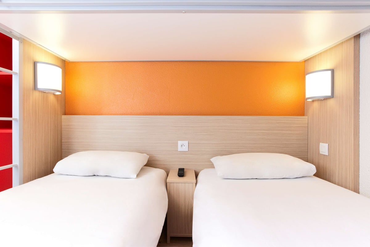 A hotel room with two beds, a wooden headboard, and a red accent wall.