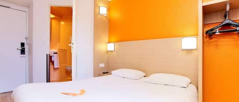 Habitación de hotel con una cama grande, cabecero de madera, dos lámparas de noche y un perchero.