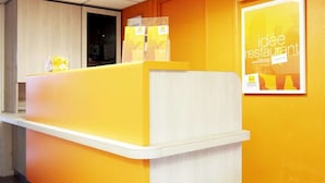 A reception desk with a yellow and white color scheme, a poster on the wall, and a door in the background. - Premiere Classe Reims Sud Bezannes (Reims)