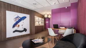 Ein moderner Empfangsbereich mit einem großen, abstrakten Gemälde, einer Rezeption und einer Sitzecke mit einer schwarzen Couch und weißen Stühlen.