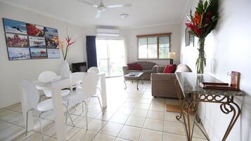 A modern living room with a dining area, a ceiling fan, and a large window with blinds.