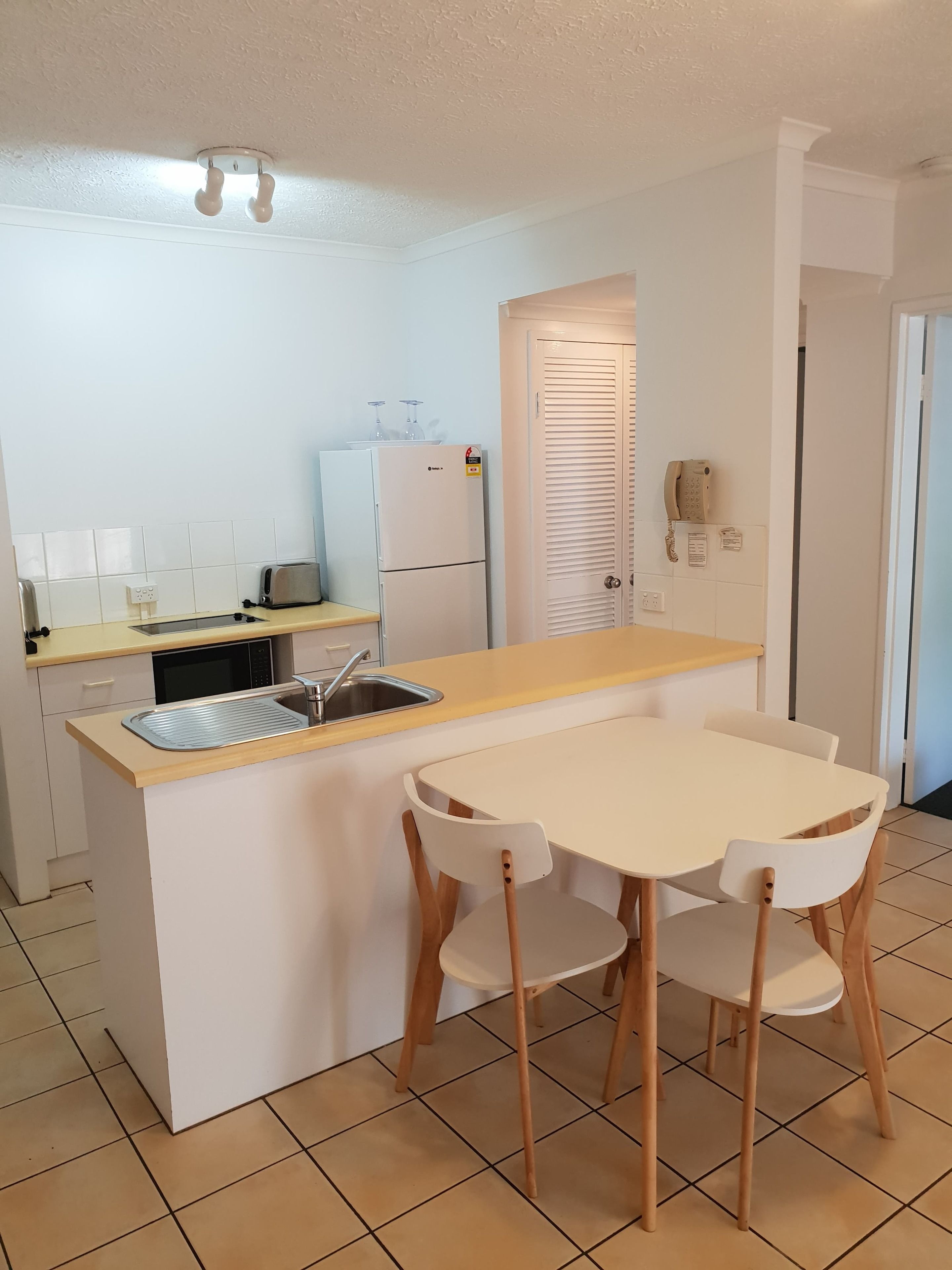 Cocina compacta con lavamanos, refrigerador, tostadora y una pequeña mesa de comedor con sillas.