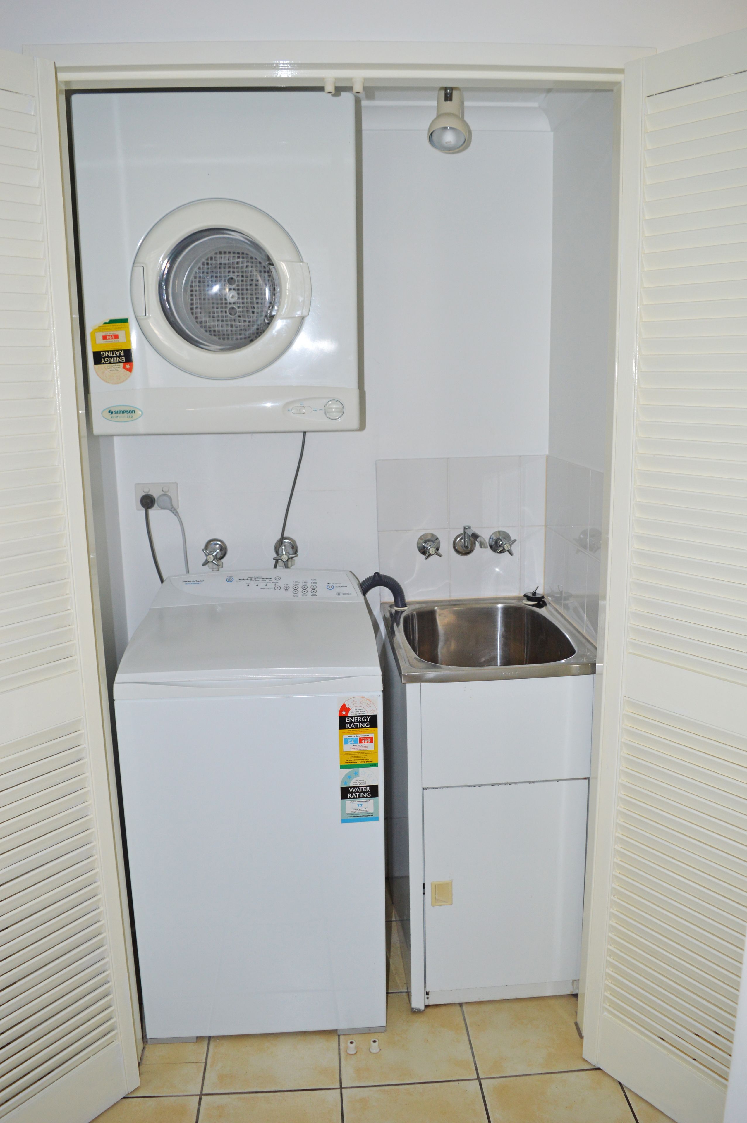 A compact laundry room with a washing machine, a sink, and a ceiling-mounted dryer.