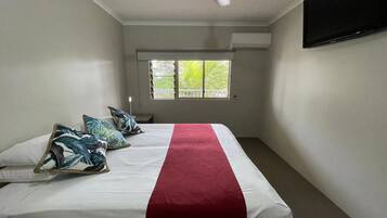 A bedroom with a bed, a ceiling fan, a window, and an air conditioning unit.