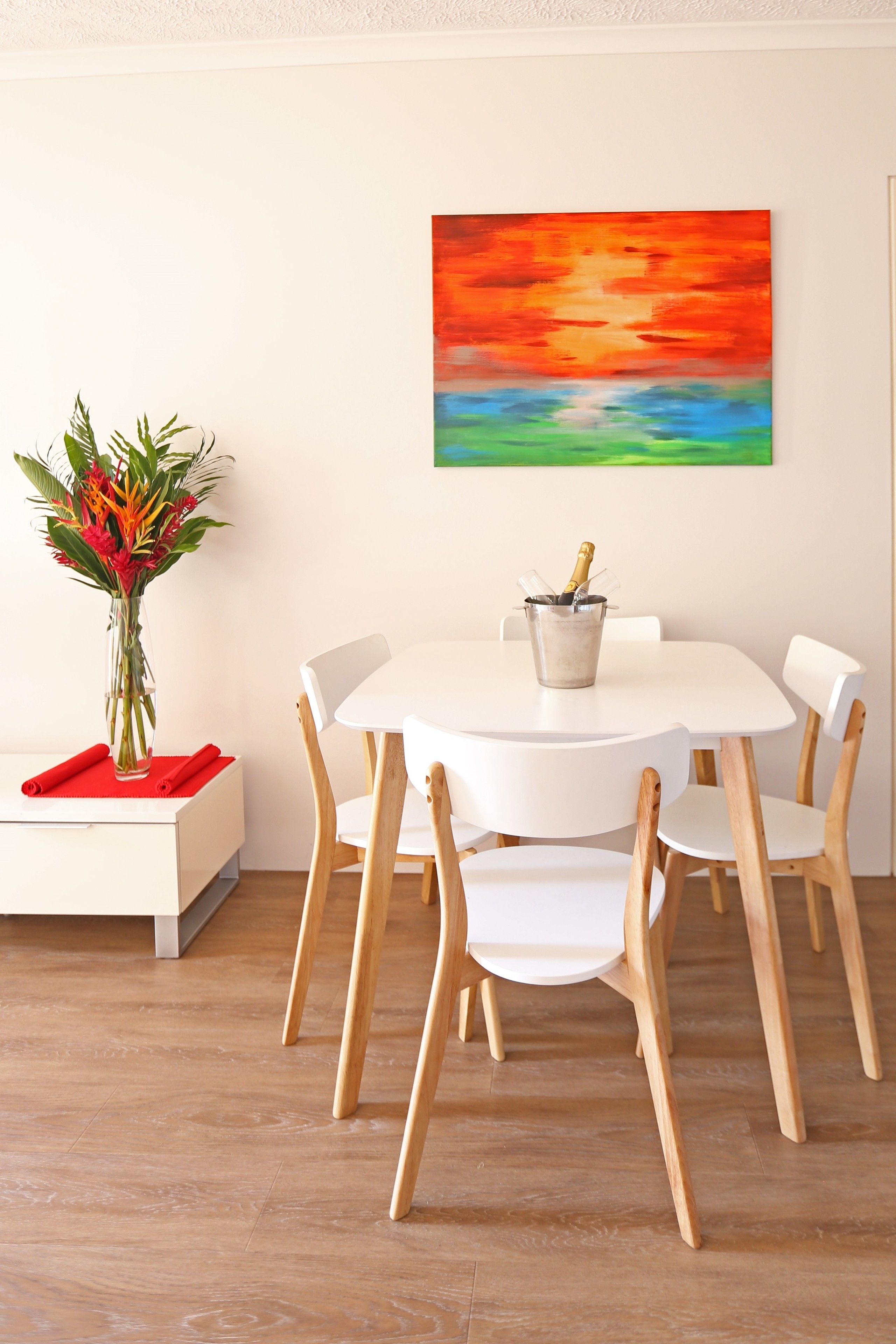 A dining area with a white table and chairs, a vase with flowers, and a painting on the wall.