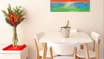 A dining area with a white table and chairs, a vase with flowers, and a painting on the wall.