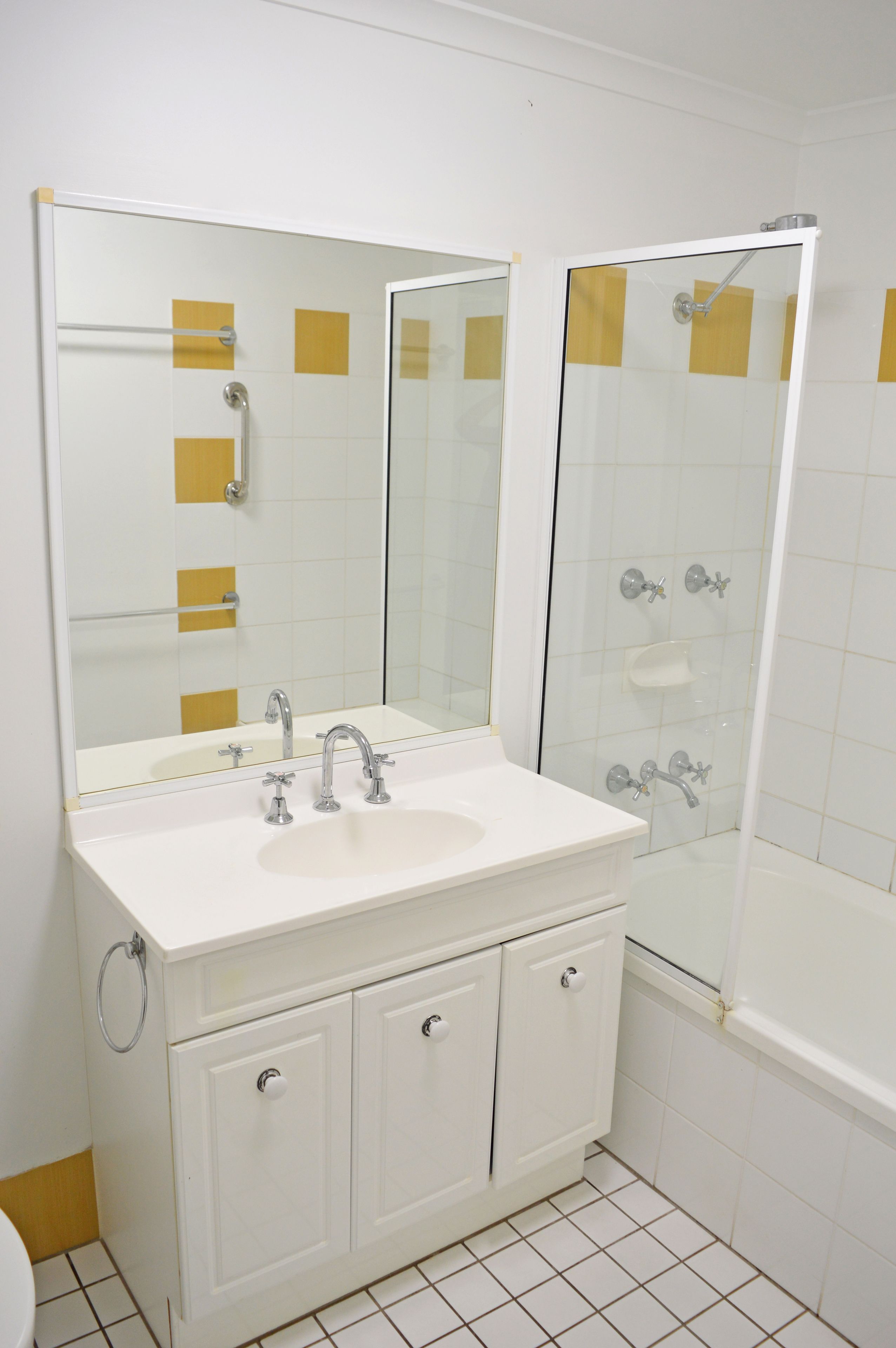 A bathroom with a white sink, two cabinets, a mirror, and a glass-enclosed shower.