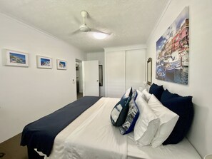 A bedroom with a bed, a ceiling fan, and a painting of a canal scene.