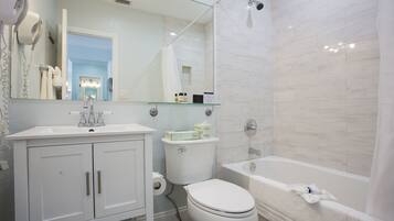 Un baño moderno con lavamanos, mueble de tocador, inodoro y bañera blancos.