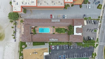 An aerial view of a building with a swimming pool, parking lot, and adjacent beach.