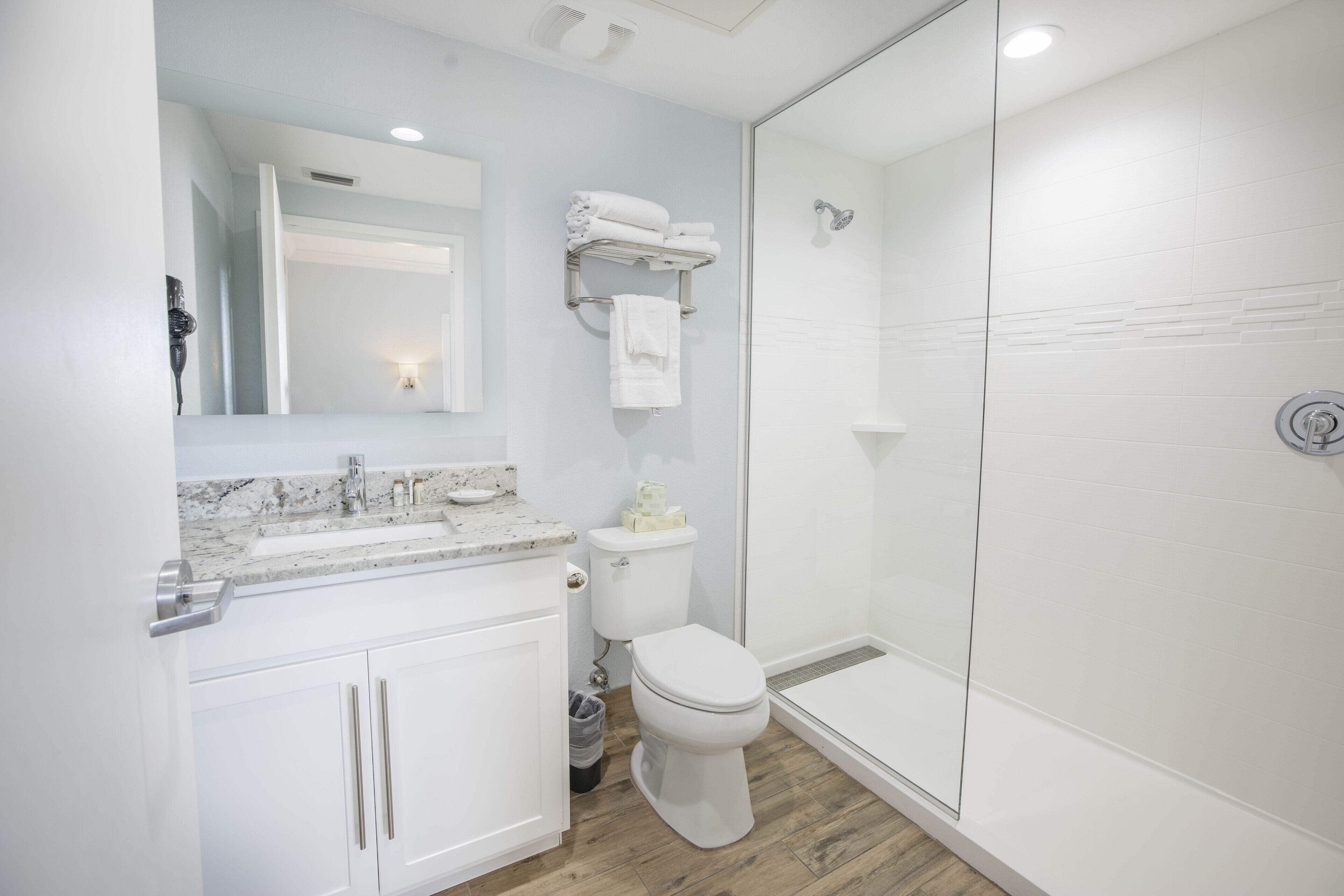 A modern bathroom with a glass shower enclosure, white fixtures, and a marble countertop.