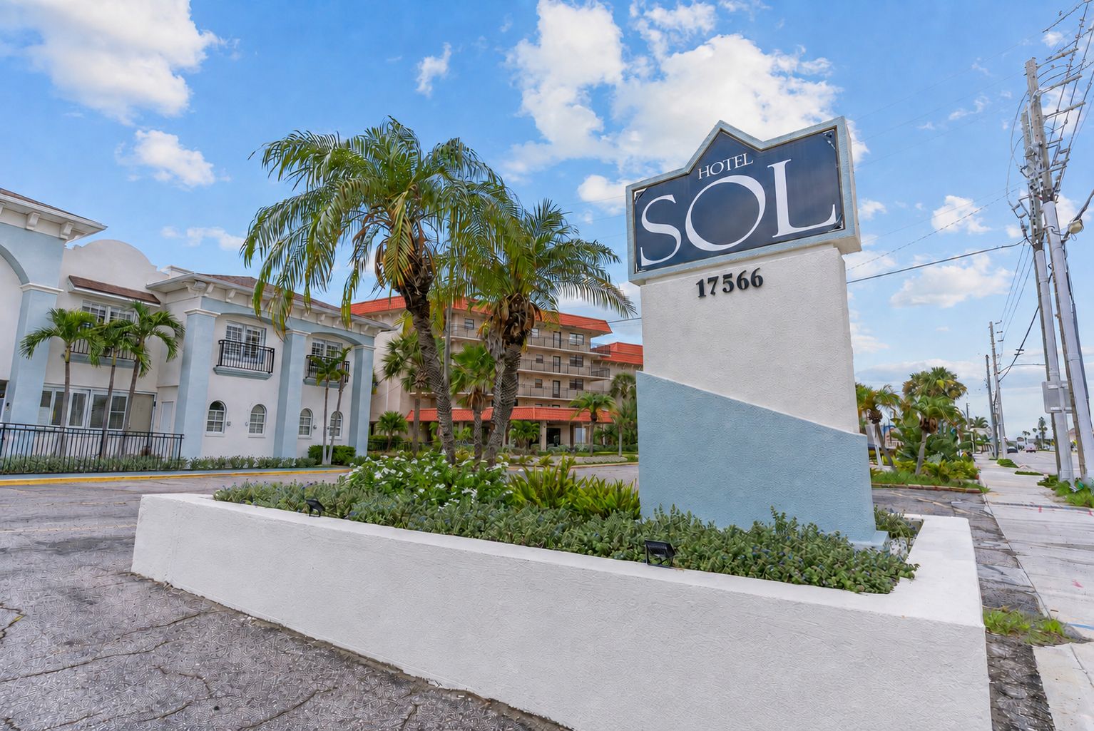 Un letrero de hotel con el nombre 'HOTEL SOL' y el número '17566' en un entorno urbano moderno, con palmeras y edificios al fondo.