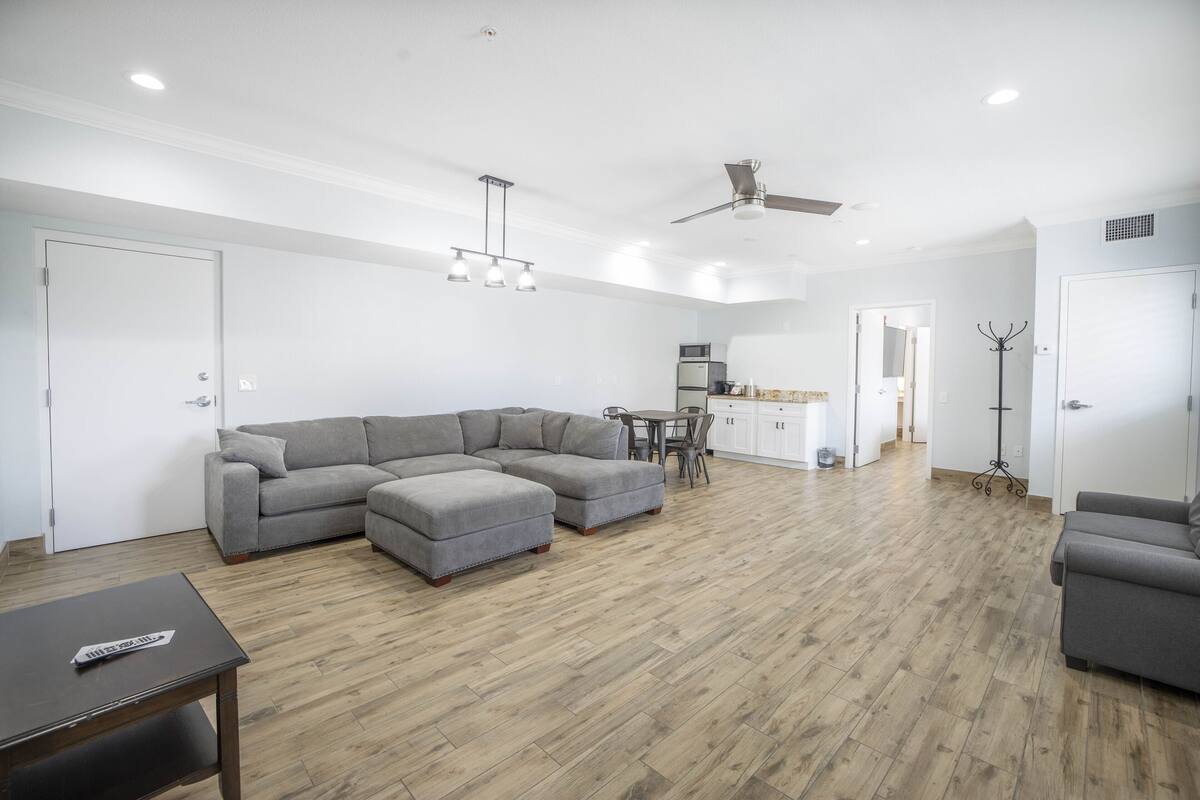 A spacious living area with a grey sectional sofa, a dining table, and a ceiling fan.
