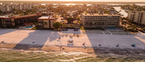 An aerial view of a beach resort with multiple buildings, a swimming pool, and a sandy beach.
