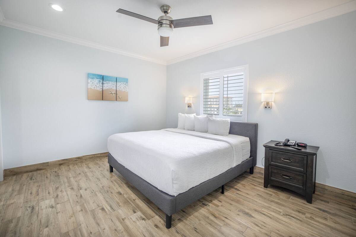 A bedroom with a bed, a nightstand, a ceiling fan, and a window with blinds.