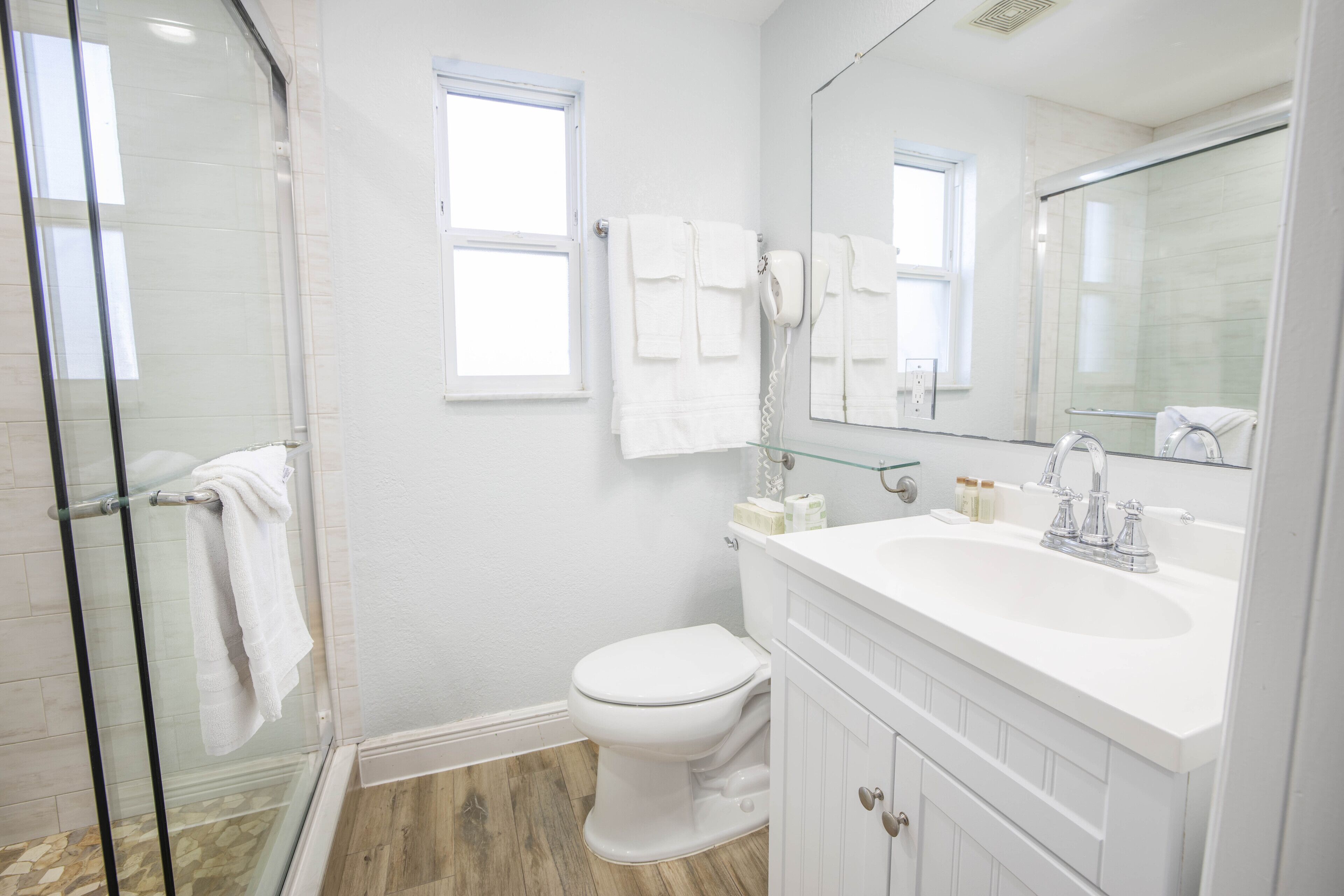 Un baño moderno con cabina de ducha de vidrio, inodoro blanco y tocador con un espejo grande.