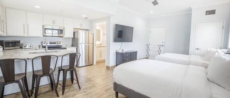 A modern hotel room with a large bed, a small kitchen area with a microwave, toaster, and refrigerator, and a TV mounted on the wall.
