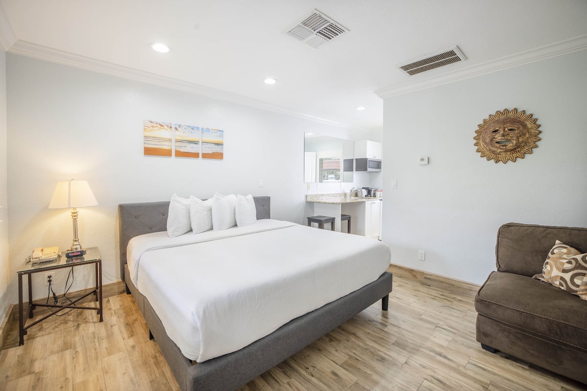 A bedroom with a bed, bedside table, lamp, and a brown sofa.