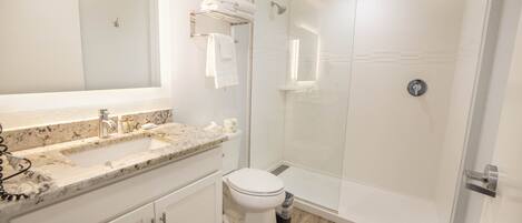 A modern bathroom with a glass-enclosed shower, a sink with a marble countertop, and a toilet.
