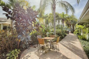 Un patio empedrado con una mesa y sillas, rodeado de plantas tropicales y palmeras.