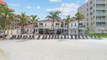 A beachfront hotel with multiple balconies, sun loungers, and palm trees.