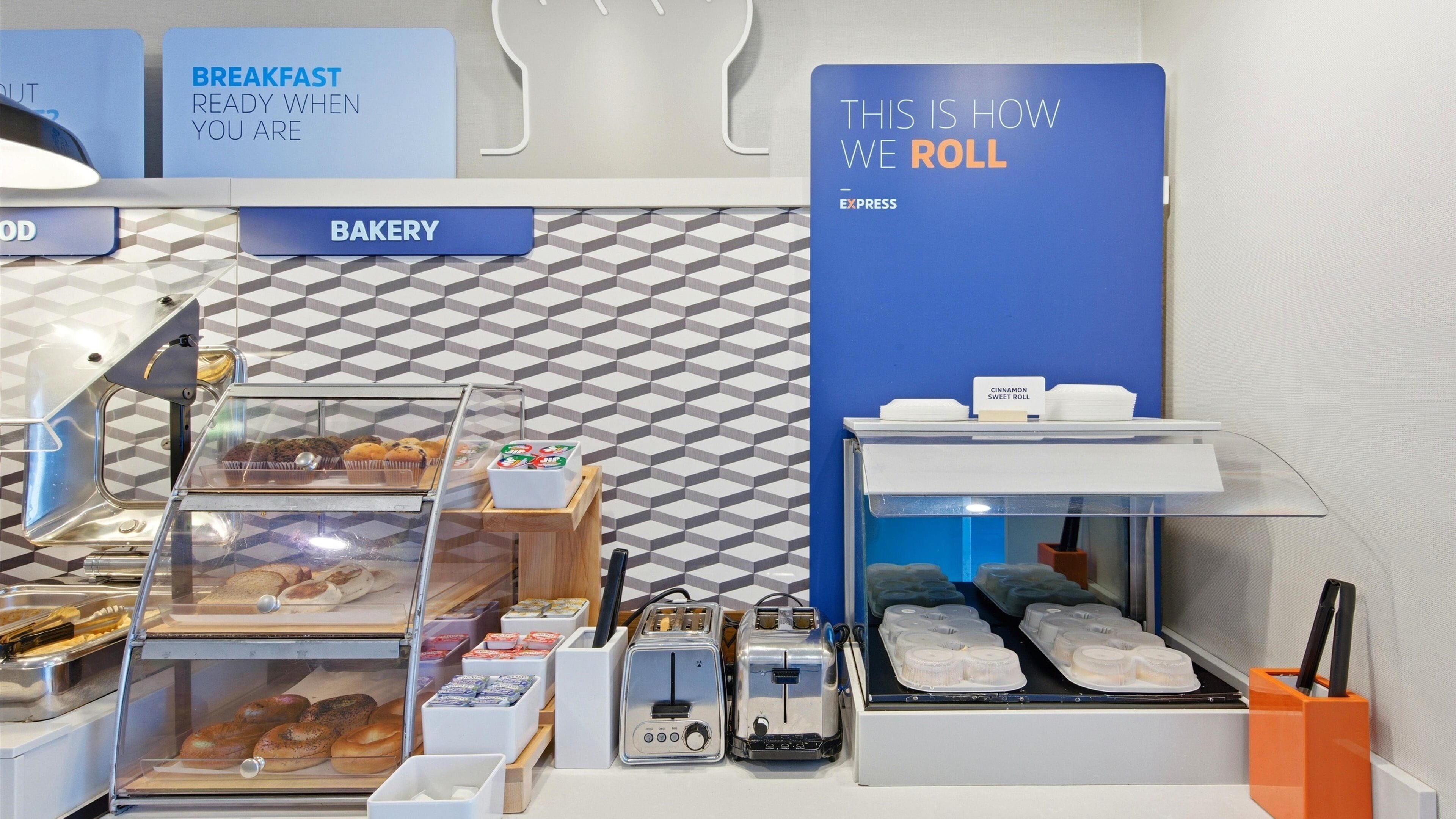 Un rayon boulangerie proposant divers produits de boulangerie, des grille-pain et un panneau indiquant que le petit-déjeuner est servi.