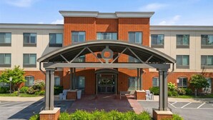 A modern building with a brick facade, a covered entrance with a circular design, and a parking lot in front. - Holiday Inn Express & Suites Bethlehem Arpt-Allentown Area (Bethlehem)