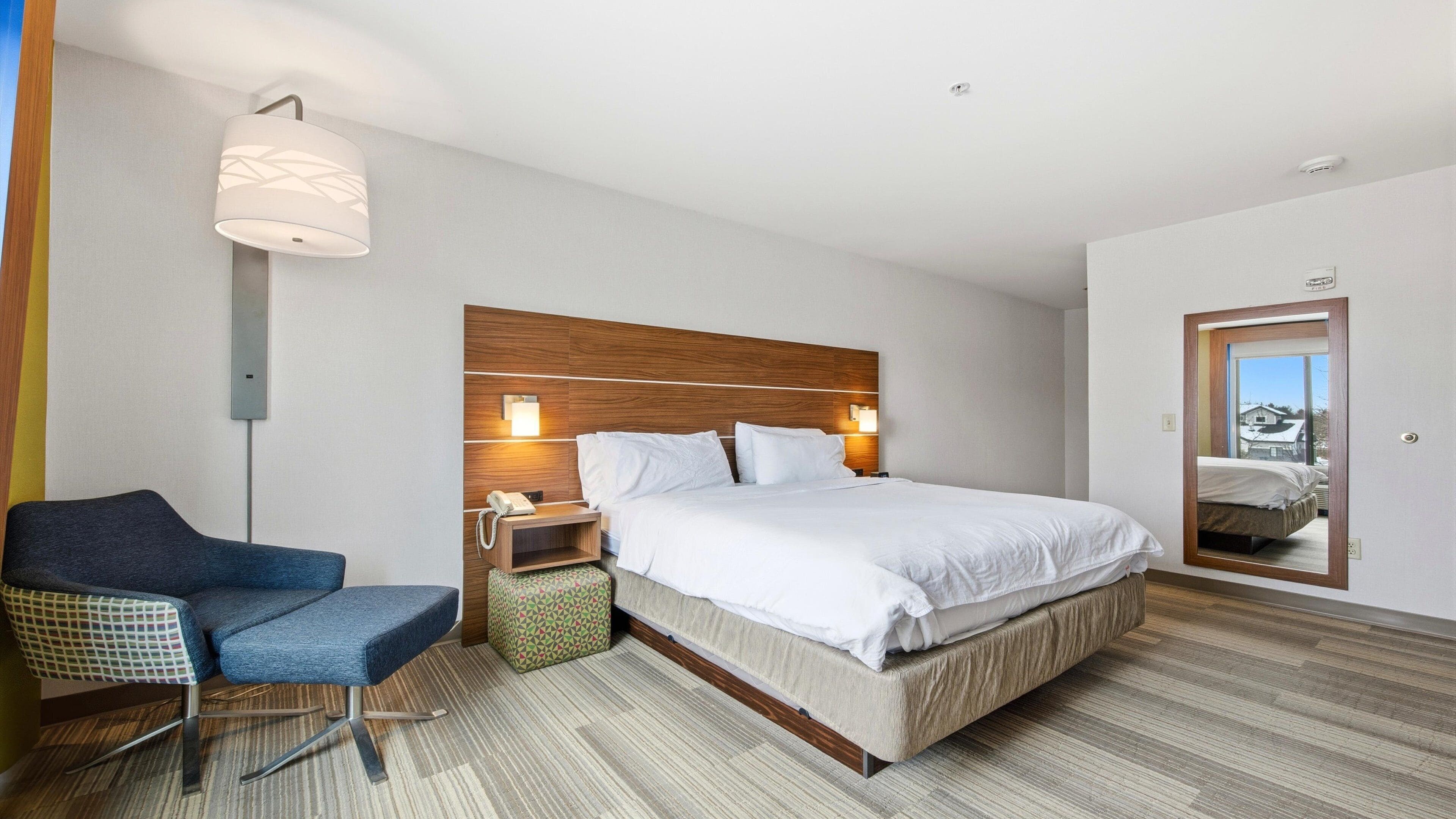 Ein Hotelzimmer mit einem großen Bett, einem Schreibtisch mit Stuhl, einem Nachttisch mit Lampe und einem Spiegel an der Wand.