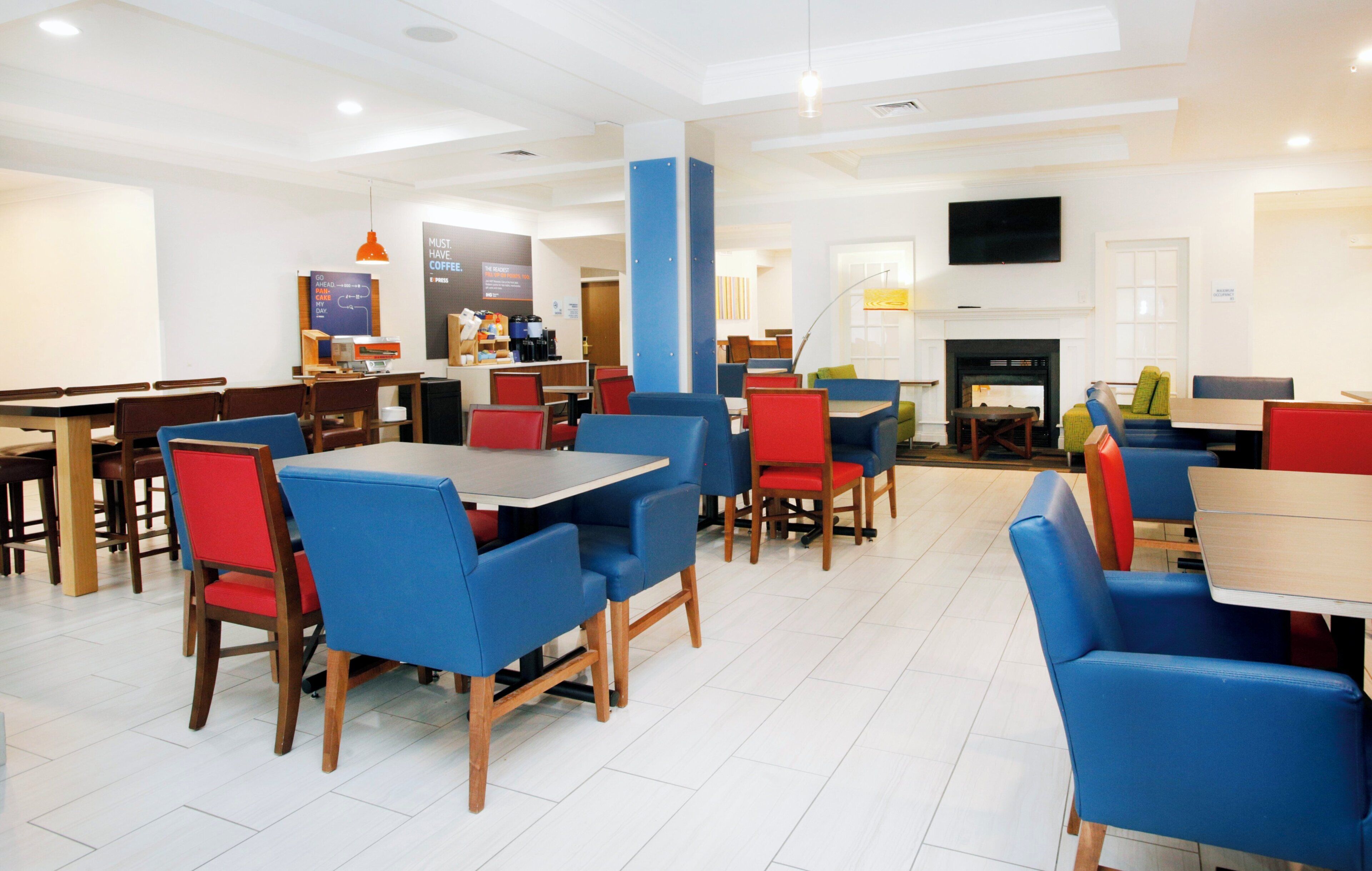 A spacious indoor dining area with multiple tables and chairs, a coffee station, and a television mounted on the wall.