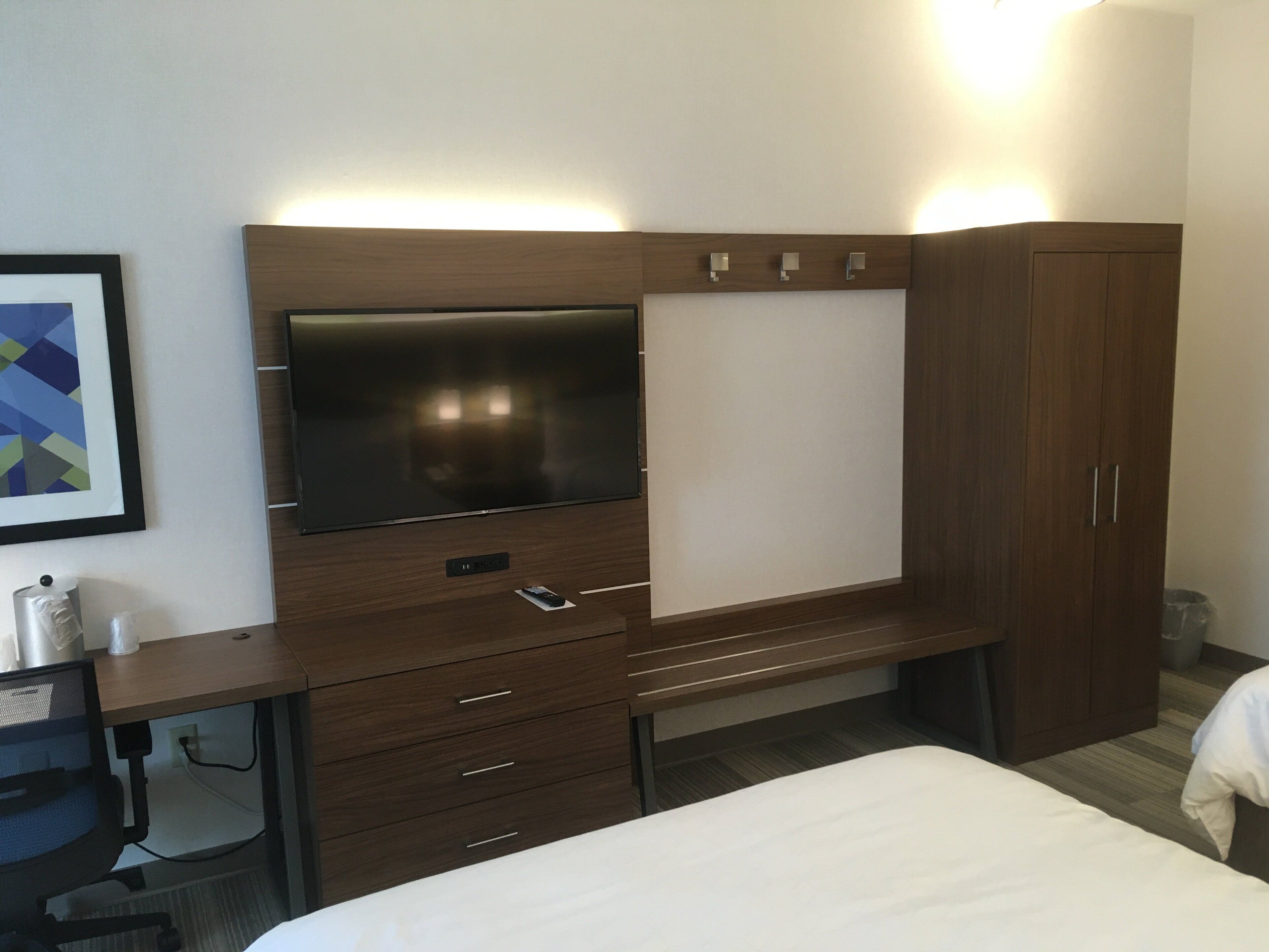 A hotel room with a bed, a desk with a chair, a TV, and a wardrobe.