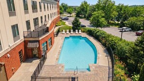 A swimming pool with a brick and glass building adjacent to it, surrounded by greenery and a parking area. - Holiday Inn Express & Suites Bethlehem Arpt-Allentown Area (Bethlehem)