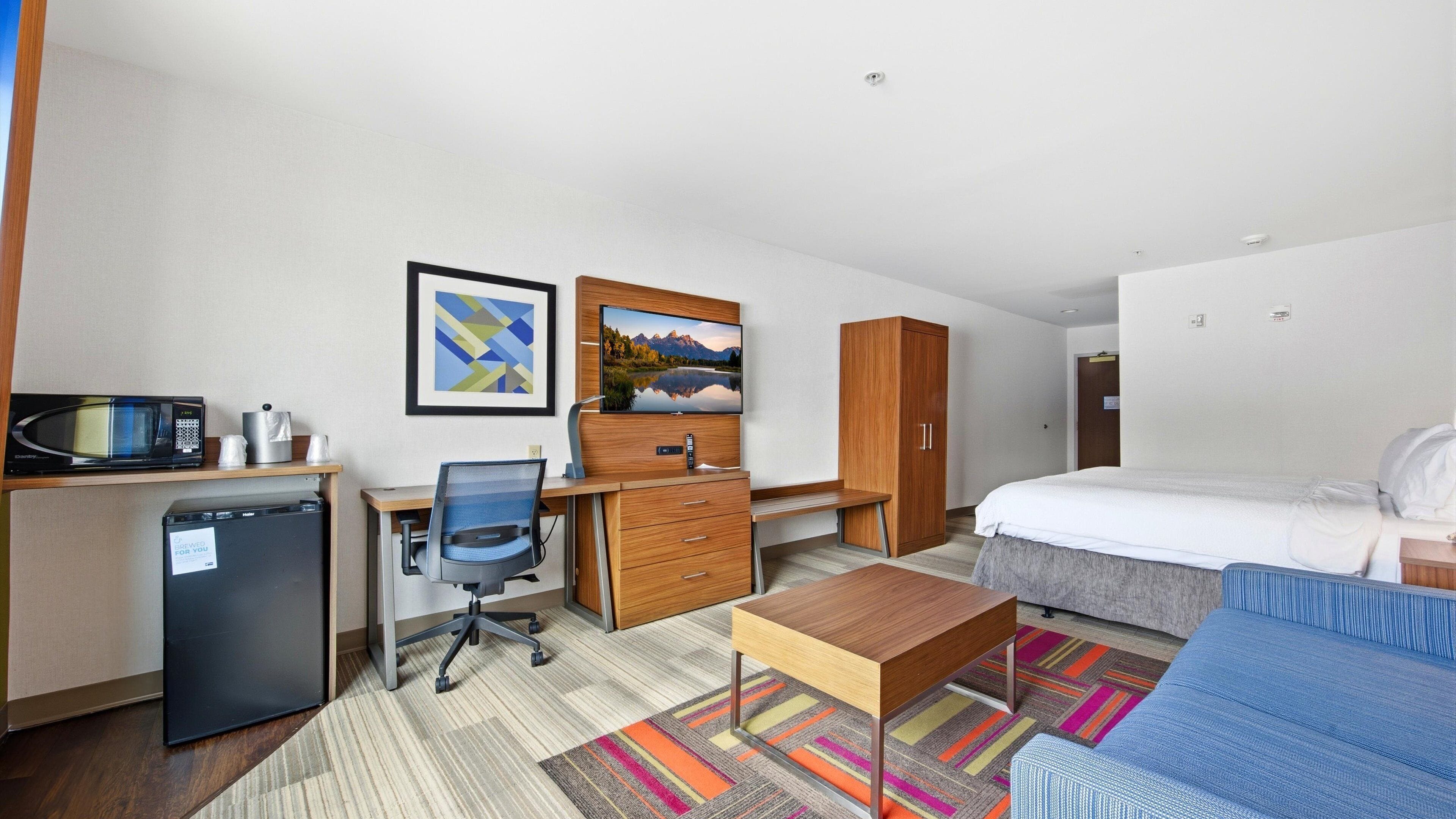 A hotel room with a bed, desk, chair, microwave, and a small refrigerator.