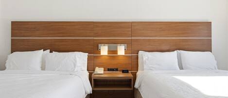 Ein Hotelzimmer mit zwei Betten, einem hölzernen Kopfteil, Nachttischlampen, einem Telefon und einer digitalen Uhr.