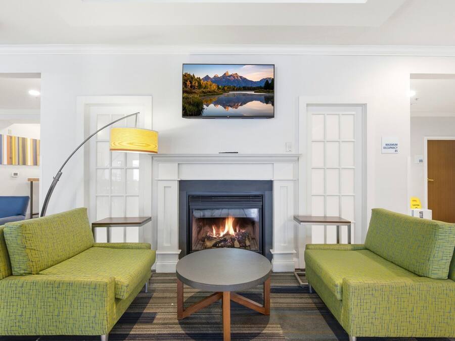 Una sala de estar moderna con sofás tapizados en verde, una mesa redonda de centro, una chimenea y un cuadro de paisaje grande sobre la repisa.