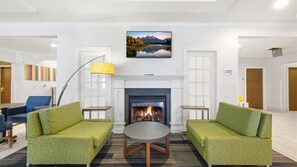 A modern living room with green upholstered sofas, a round coffee table, a fireplace, and a large landscape painting above the mantel.