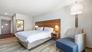 Una habitación de hotel moderna con una cama grande, una mesita de noche con lámpara, un pequeño rincón de descanso y un cabecero de madera.