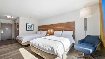 A hotel room with two beds, a blue armchair, a wooden headboard, and a framed picture on the wall.