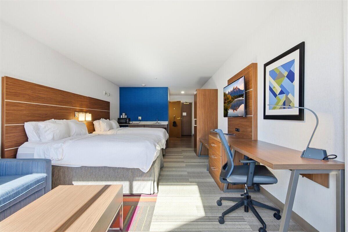 A hotel room with a bed, a desk, a chair, a sofa, and a bathroom visible in the background.