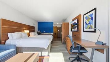 A hotel room with a bed, a desk, a chair, a sofa, and a bathroom visible in the background.