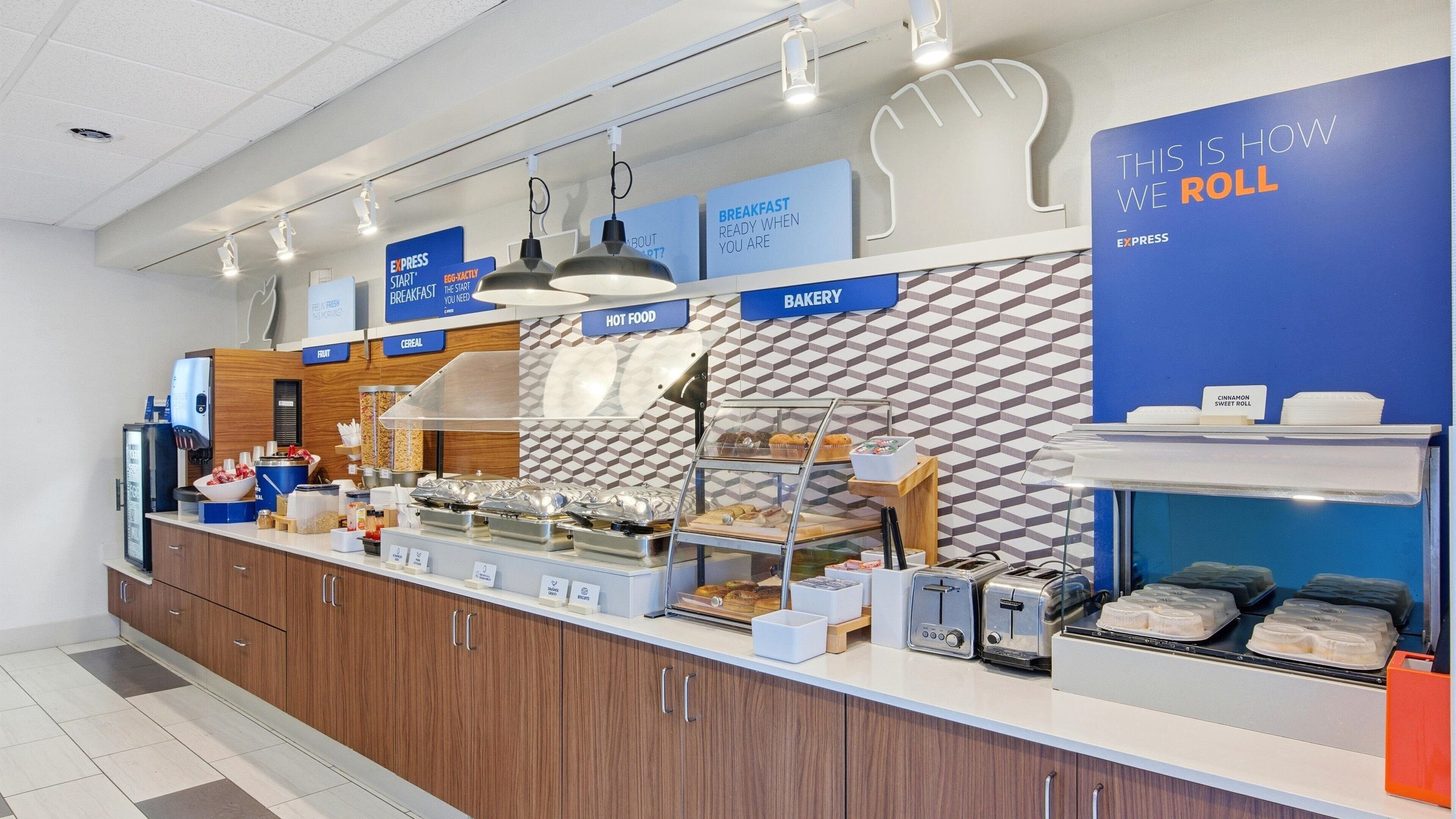A breakfast buffet area with labeled sections for hot food, bakery, and cereal.