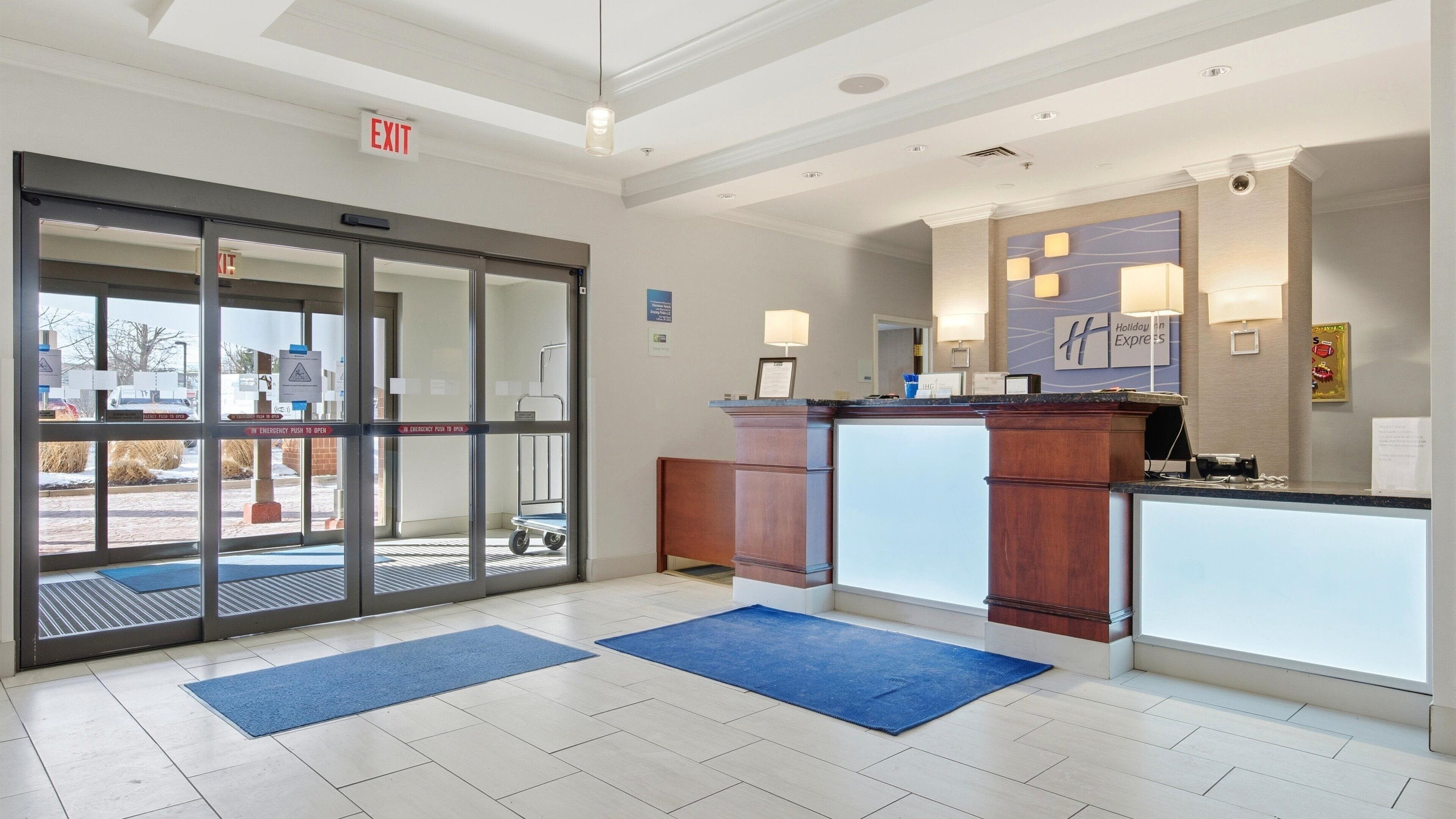 A hotel reception area with a glass door entrance, a reception desk, and a blue mat in front.