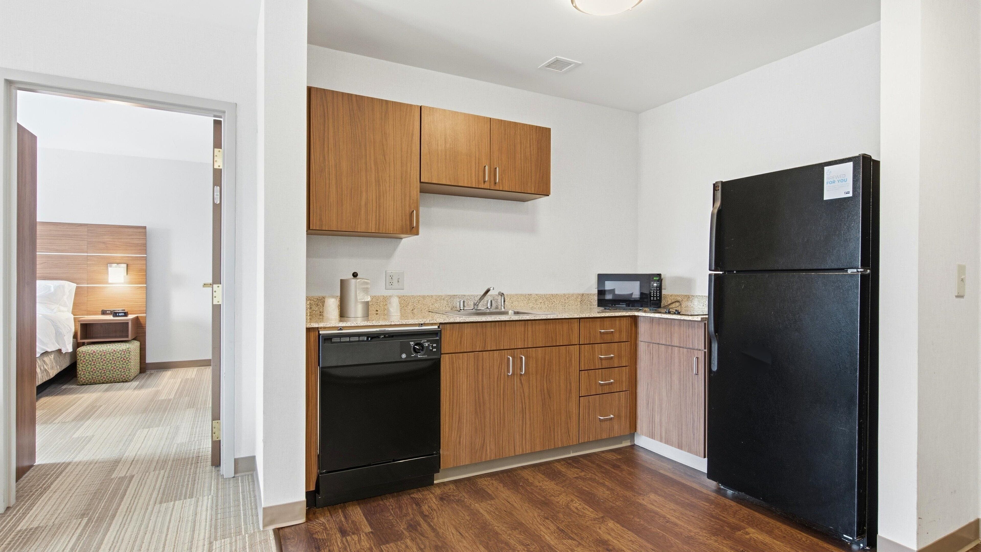 A compact kitchen with wooden cabinets, a black refrigerator, a microwave, and a dishwasher.